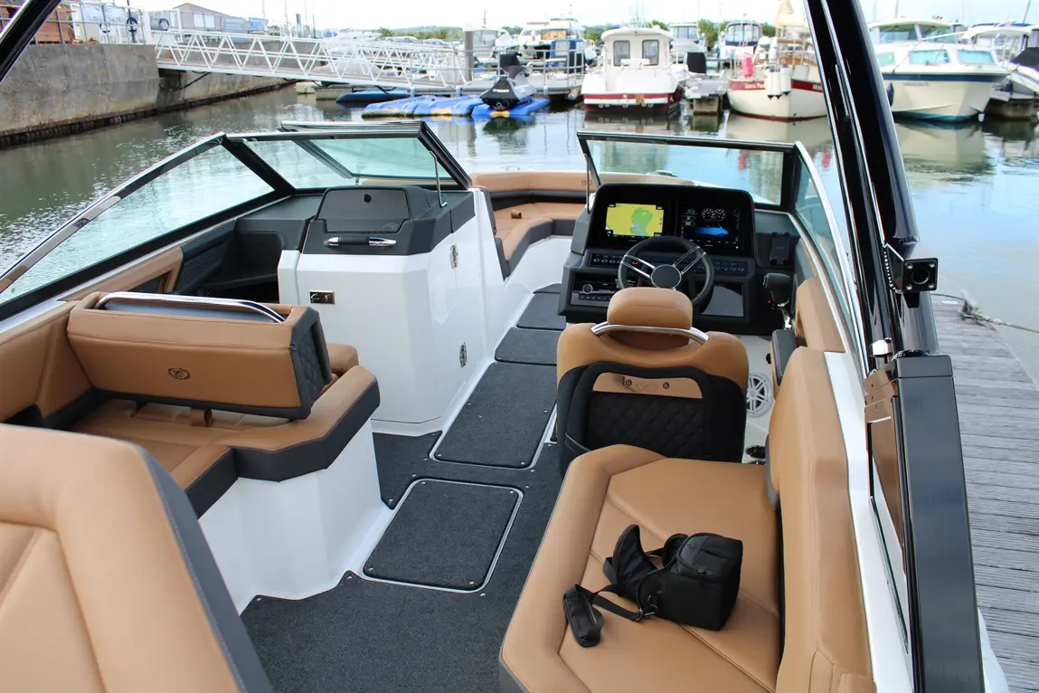 Interior of a modern boat with tan leather seating, dashboard with screens, and a view of the marina and boats outside.